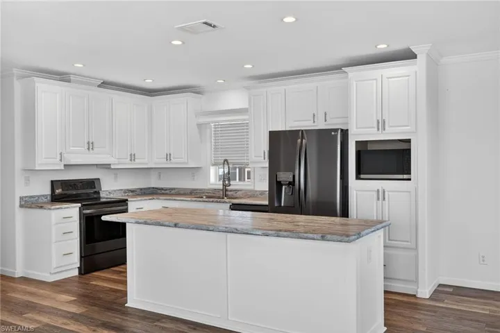 Kitchen featuring stainless steel appliances, white cabinets, LVP floors, a kitchen island, and recessed lighting