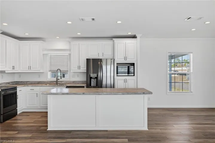 Kitchen with white cabinets, stainless steel appliances, crown molding, LVP floors, and recessed lighting