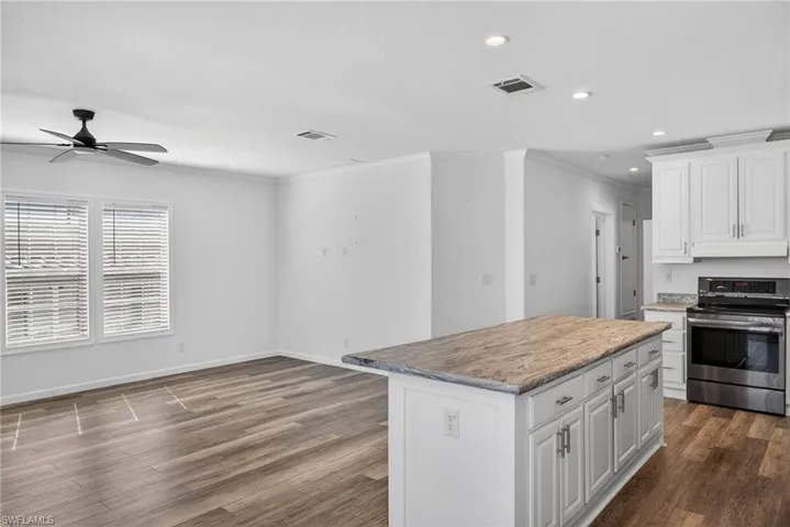 Kitchen with white cabinetry, stainless steel electric range oven, a center island, ornamental molding, and ceiling fan