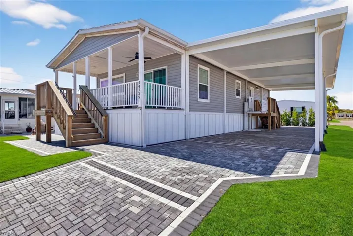 Manufactured home with a front yard, a carport, a porch, and decorative paver driveway