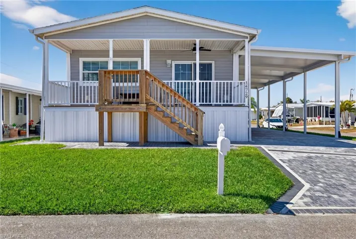 Manufactured home featuring a front yard, covered porch, driveway, and an attached carport