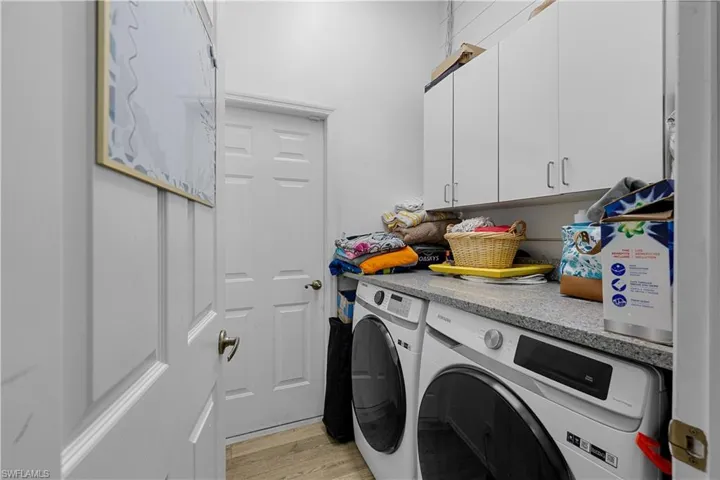 Clothes washing area with cabinets, washing machine and dryer, and light hardwood / wood-style floors