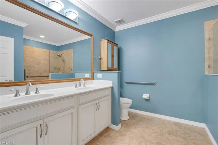 Bathroom featuring a tile shower, crown molding, and double vanity