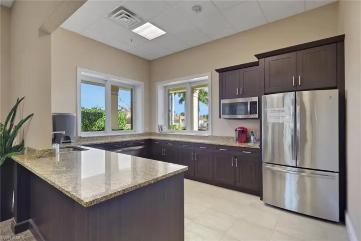 Kitchen featuring stainless steel appliances, light stone countertops, dark brown cabinetry, a peninsula, and a drop ceiling