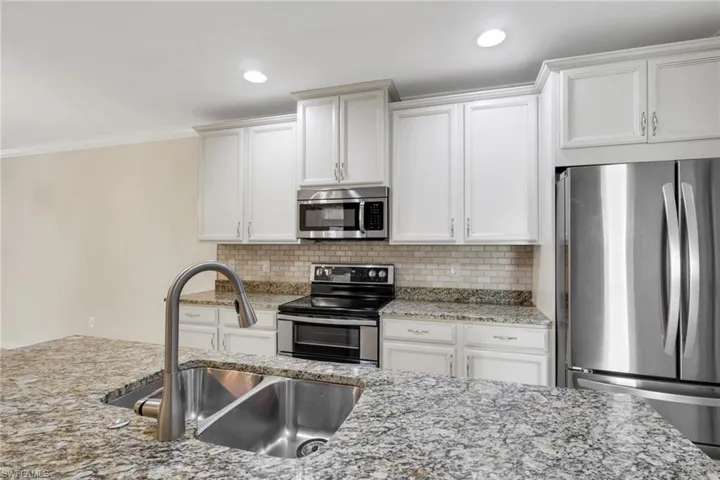 Kitchen with appliances with stainless steel finishes, light stone counters, white cabinetry, ornamental molding, and recessed lighting