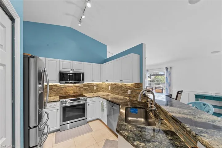Kitchen with white cabinetry, stainless steel appliances, dark stone counters, light tile patterned floors, and lofted ceiling