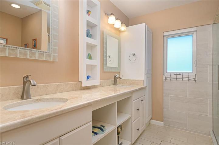 Shared hallway bathroom with shower, double vanities, and toilet