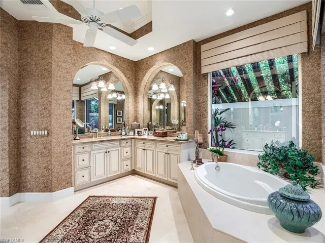 Bathroom featuring a relaxing tiled bath, a healthy amount of sunlight, ceiling fan, tile flooring, and large vanity