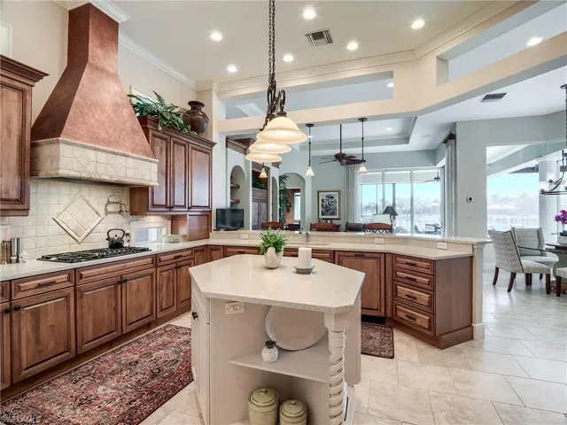 Kitchen featuring hanging light fixtures, gas stovetop, kitchen peninsula, backsplash, and custom exhaust hood