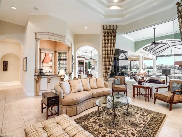 Living room with a towering double tray ceiling with crown molding, mitered glass windows and light tile floors