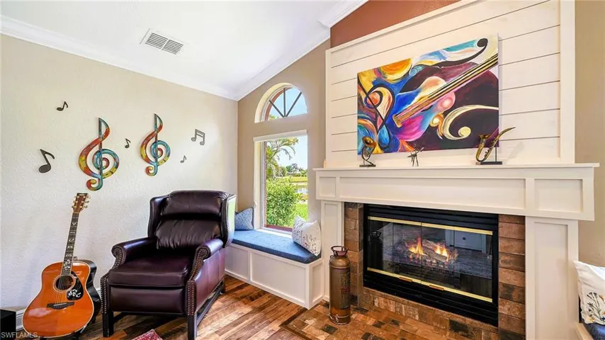 Living area featuring crown molding, vaulted ceiling, a glass covered fireplace, and wood finished floors