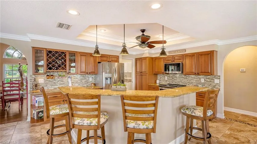 Kitchen with stainless steel appliances, arched walkways, brown cabinetry, crown molding, and a raised ceiling