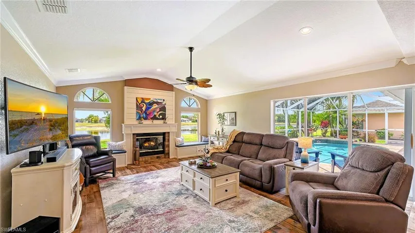 Living area featuring ceiling fan, light wood-style flooring, ornamental molding, healthy amount of natural light, and lofted ceiling