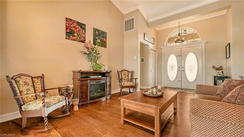 Living area with wood finished floors, crown molding, baseboards, a high ceiling, and french doors