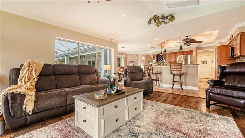 Living room with dark wood finished floors, ornamental molding, a ceiling fan, and vaulted ceiling