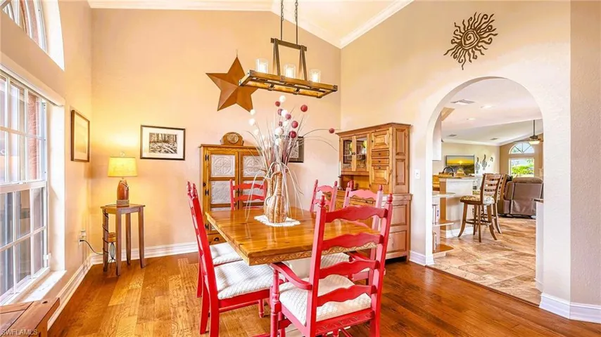 Dining area with arched walkways, wood finished floors, crown molding, baseboards, and high vaulted ceiling