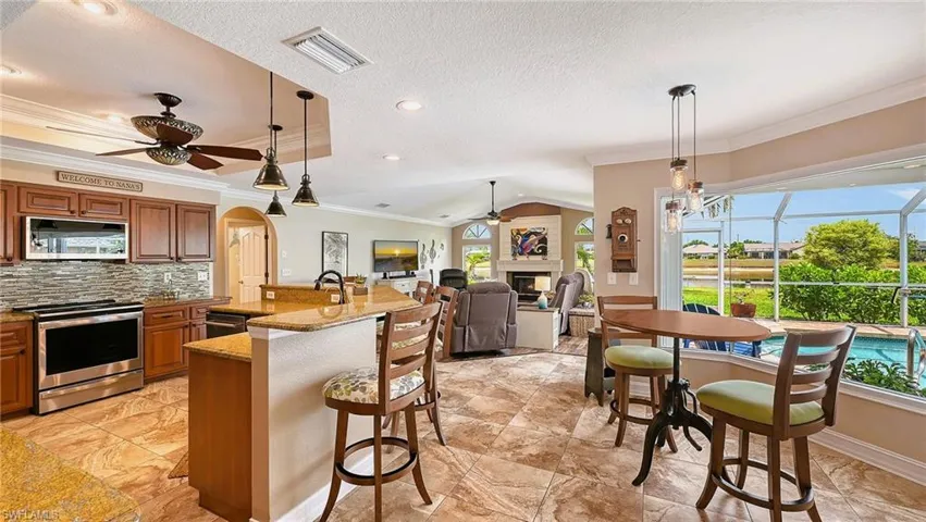 Kitchen with a ceiling fan, stainless steel appliances, crown molding, brown cabinetry, and a glass covered fireplace