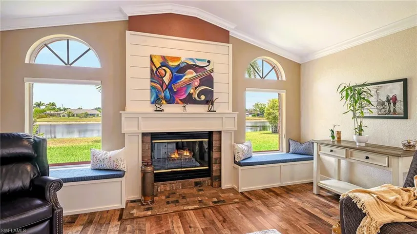 Living area featuring a water view, wood finished floors, a glass covered fireplace, vaulted ceiling, and healthy amount of natural light