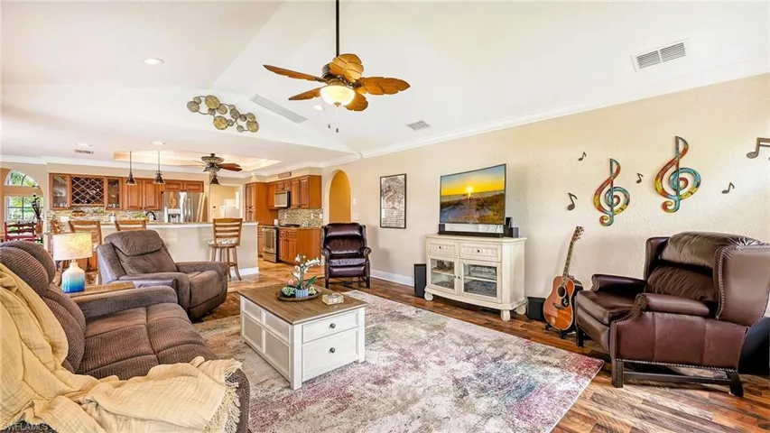Living room with a ceiling fan, vaulted ceiling, light wood-style flooring, ornamental molding, and arched walkways