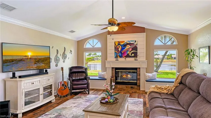 Living area featuring ceiling fan, wood finished floors, a glass covered fireplace, a water view, and vaulted ceiling