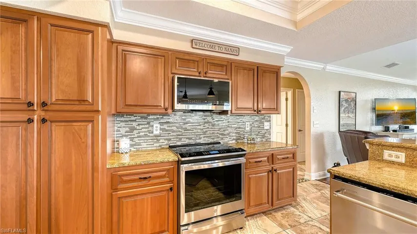 Kitchen with appliances with stainless steel finishes, crown molding, arched walkways, tasteful backsplash, and light stone countertops