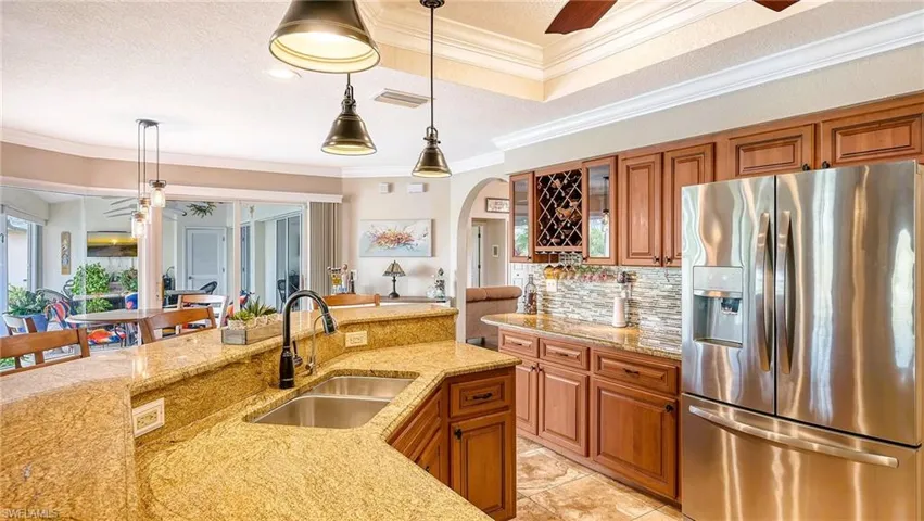 Kitchen featuring stainless steel refrigerator with ice dispenser, a sink, ornamental molding, arched walkways, and light stone countertops