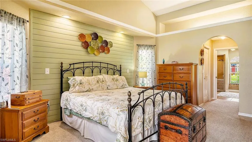 Bedroom featuring light carpet, arched walkways, lofted ceiling, baseboards, and ensuite bathroom