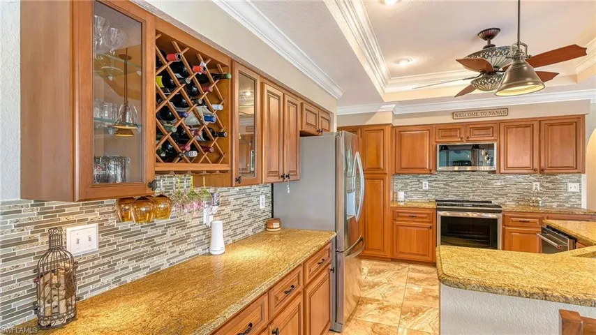 Kitchen with appliances with stainless steel finishes, ornamental molding, a tray ceiling, backsplash, and ceiling fan