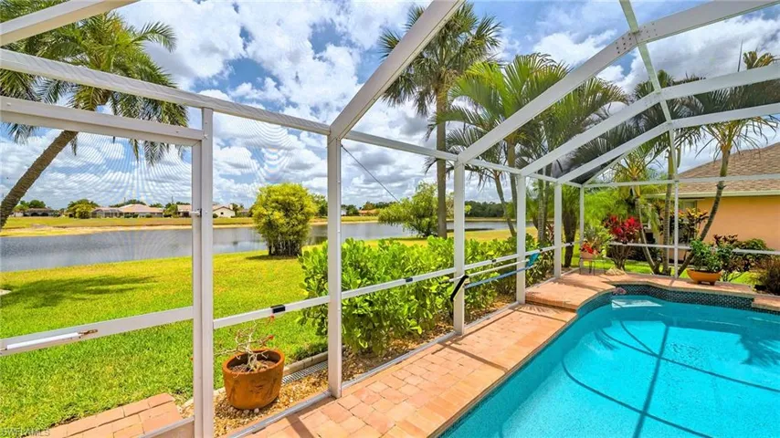 Swimming pool with a water view, glass enclosure, a lawn, and a patio area