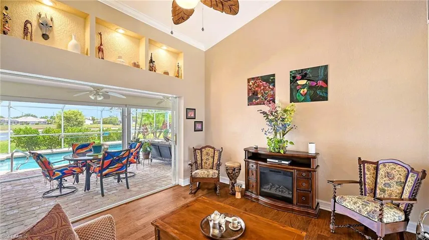 Living area featuring a ceiling fan, ornamental molding, a sunroom, wood finished floors, and a towering ceiling