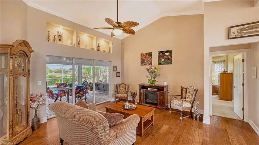 Living area with a ceiling fan, crown molding, wood finished floors, baseboards, and high vaulted ceiling