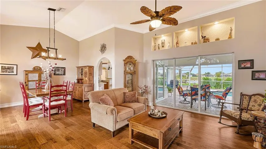Living room with high vaulted ceiling, arched walkways, wood finished floors, ceiling fan, and baseboards