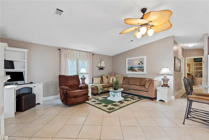 Tiled living room featuring ceiling fan, built in features, lofted ceiling