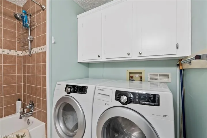 Laundry area with washer and clothes dryer, a textured ceiling, and cabinets