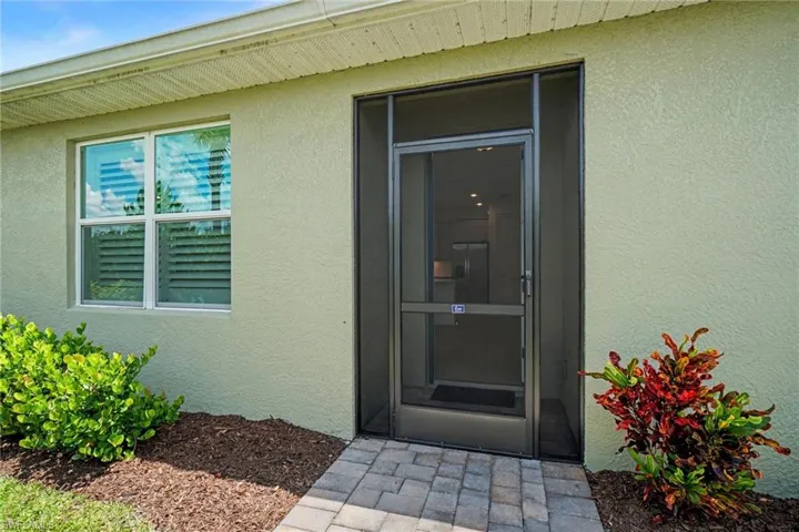 Entryway featuring a screened door, stucco exterior, and a paver walkway