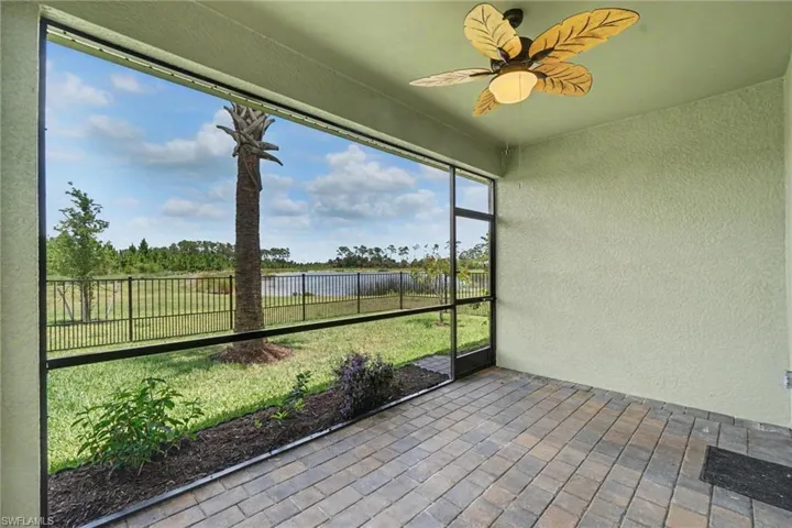 Screened outdoor living area featuring a decorative ceiling fan, brick paver flooring, stucco walls, and a private rear yard with a water feature