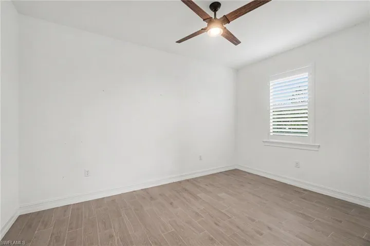 GlSS FRENCH DOORS Bright room featuring a ceiling fan with integrated lighting, a single window with plantation shutters, wood-finish flooring, and white baseboards