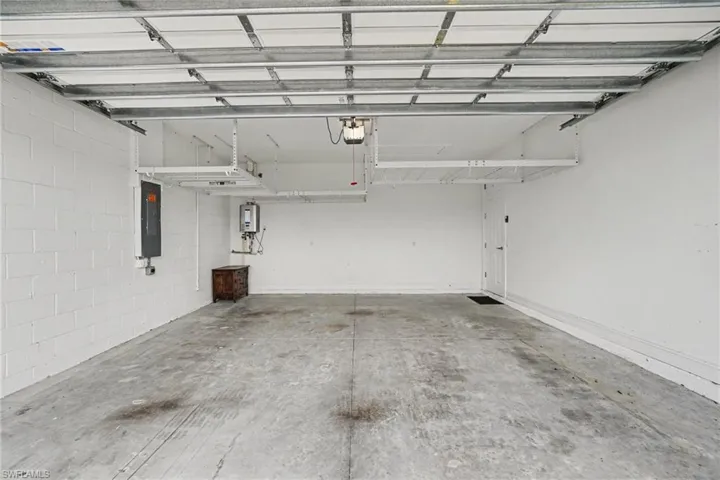 Spacious garage overhead storage featuring a concrete floor, painted block wall, white overhead storage racks, and a white interior door