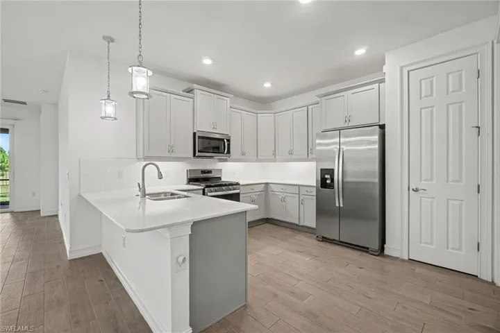Modern kitchen featuring wood-finish flooring, light-colored cabinetry, stainless steel appliances, a white countertop island, and recessed lighting