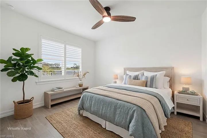 Light-filled bedroom featuring a wood-finish ceiling fan with integrated lighting, wood-finish flooring, and a large window with white plantation shutters