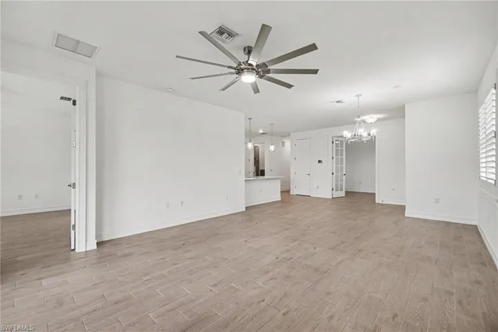 Open-concept living space with wood-look plank tile flooring throughout, featuring a large ceiling fan with brushed nickel finish, white plantation shutters, and recessed lighting