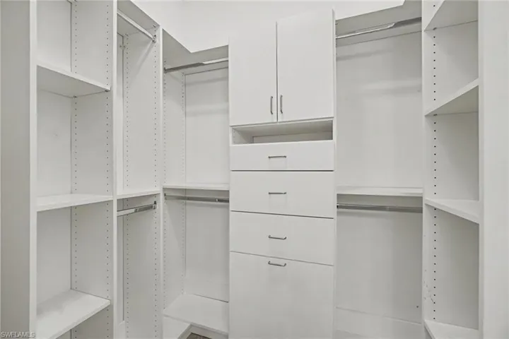 Custom white built-in closet system featuring multiple shelving units, hanging rods, and a central dresser with four drawers and upper cabinetry