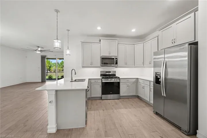Modern kitchen featuring light cabinetry, stainless steel appliances, a white countertop island with pendant lighting, and wood-finish flooring