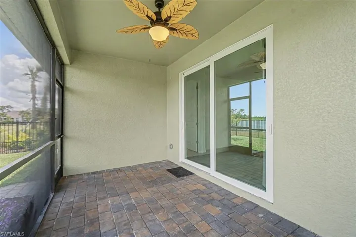 Screened outdoor area featuring a ceiling fan with leaf-shaped blades, multi-toned paver flooring, and white-framed sliding glass doors