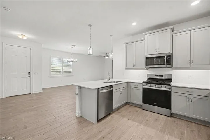 Modern kitchen featuring light gray cabinetry, stainless steel appliances, a white subway tile backsplash, and a large island with a white countertop and pendant lighting