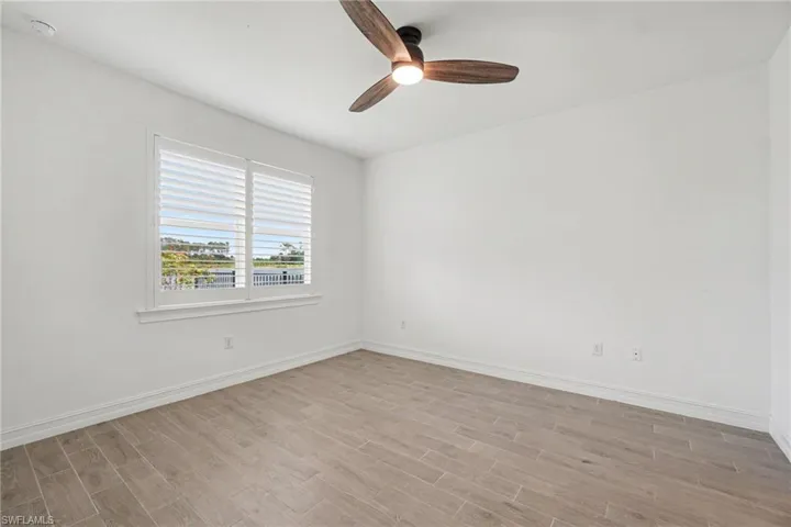 Light-filled room featuring wood-finish flooring, a contemporary ceiling fan, and a window with white plantation shutters