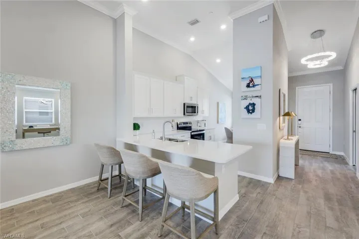 Kitchen featuring crown molding, stainless steel appliances, a chandelier, white cabinets, and a kitchen breakfast bar