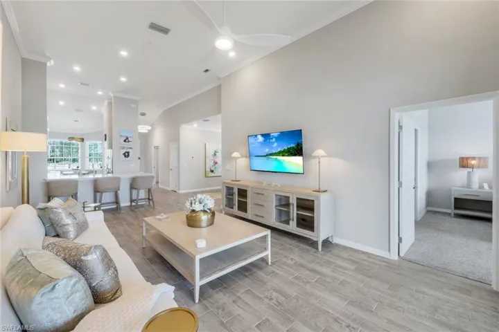 Living room featuring wood tiled floors, ornamental molding, ceiling fan, a towering ceiling, and recessed lighting