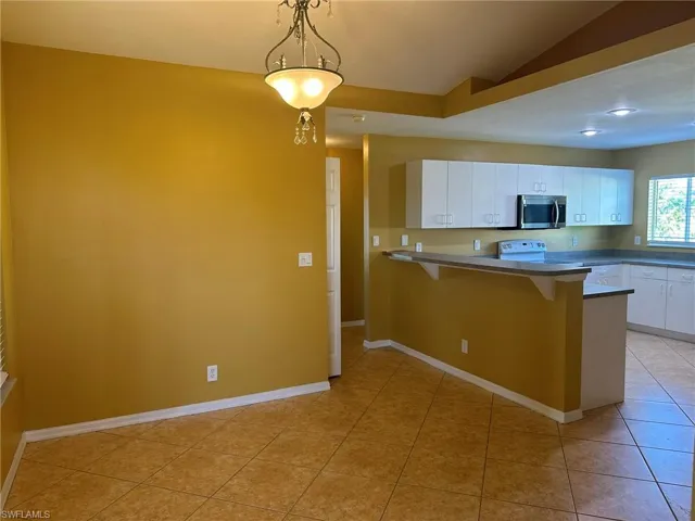 Kitchen with a peninsula, white cabinetry, a kitchen breakfast bar, pendant lighting, and stainless steel microwave