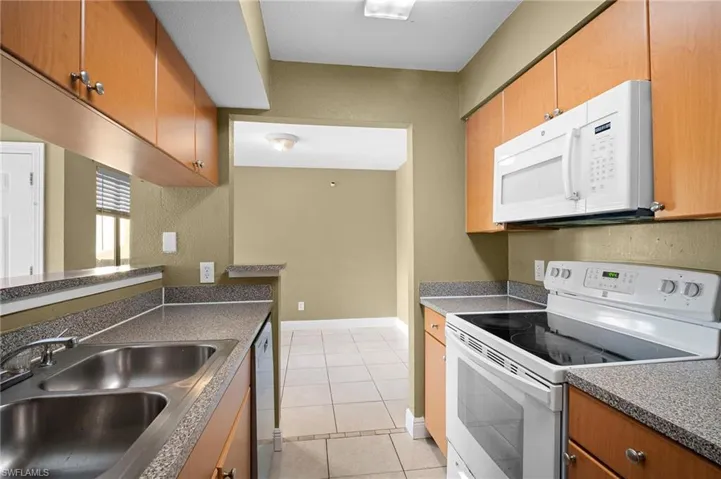 Kitchen with white appliances, light tile patterned floors, dark countertops, brown cabinets, and a textured wall